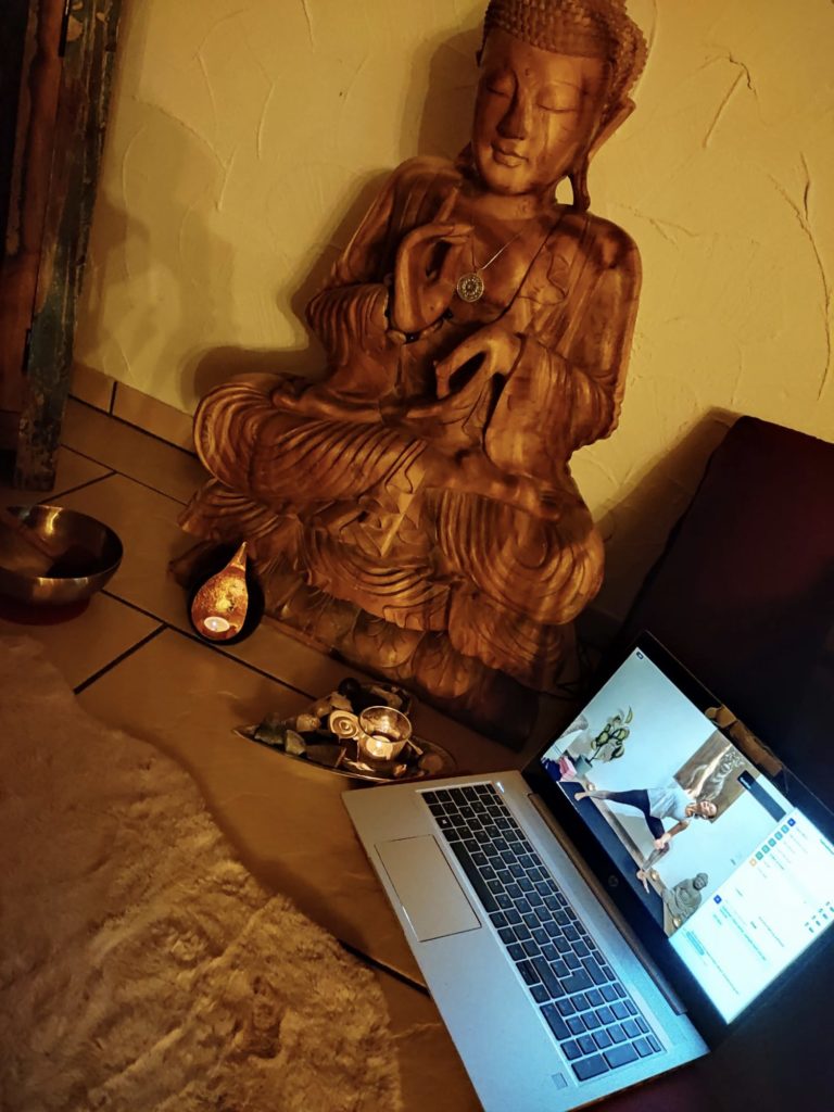 Ein Bildschirm mit Elke bei einer Online Yoga Stunde, daneben die Statue eines Buddhas