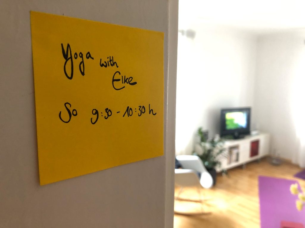 Ein Post it für einen Online Yoga Termin mit Elke, im Hintergrund ist eine Yogamatte und ein Bildschirm zu sehen