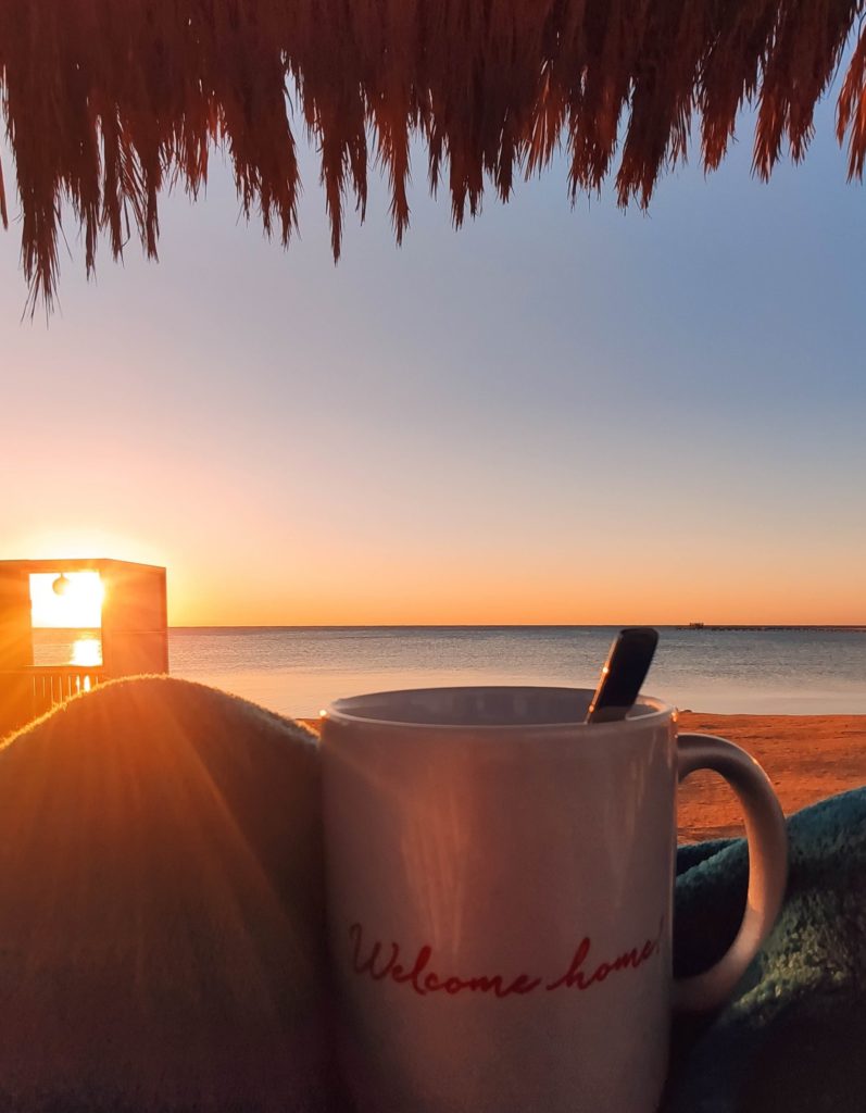 Morgens bei Sonnenaufgang mit einem Kaffee am Strand